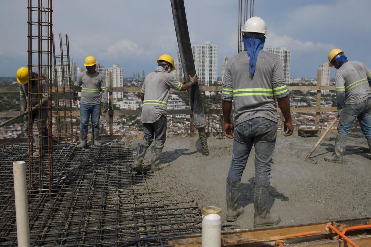 Ilustración: una cuadrilla con cascos y chalecos vacía y nivela concreto en una losa, con una ciudad al fondo